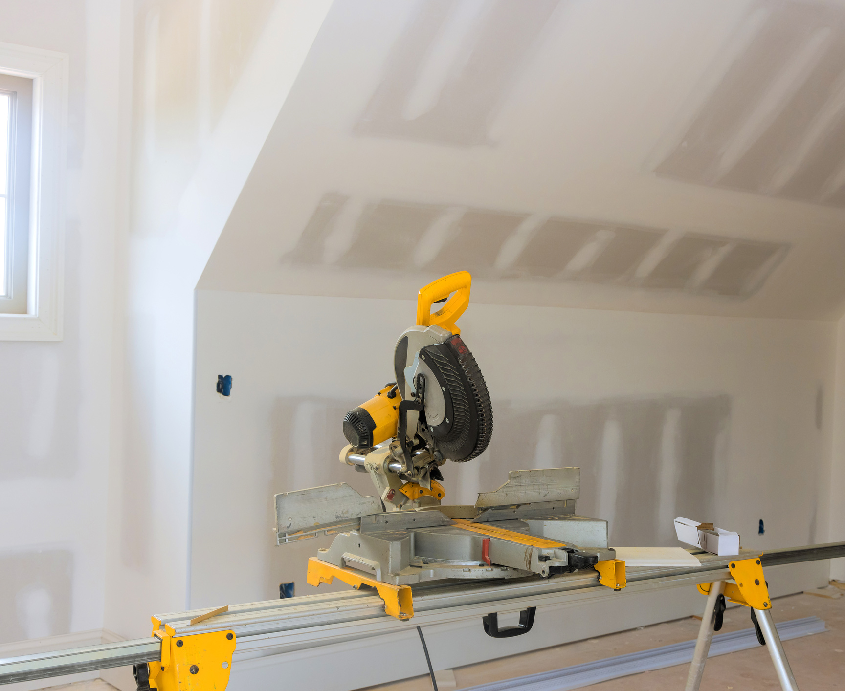 Circular saw in newly constructed room preparing for interior finishing work. Circular saw sits on stand, surrounded by drywall as workers prepare for painting finishing touches in room.
